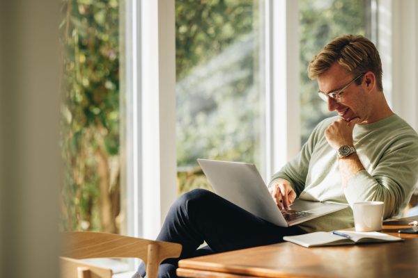 Young man using laptop and smiling Young man using laptop and smiling at home. Man sitting by table working on laptop computer.