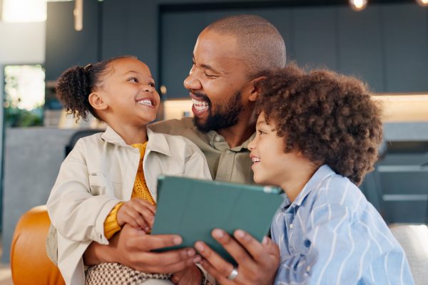 Laughing, movie and tablet with family in living room of home for bonding, entertainment or love. App, social media or streaming with happy father and children in apartment for subscription service Laughing, movie and tablet with family in living room of home for bonding, entertainment or love. App, social media or streaming with happy father and children in apartment for subscription service